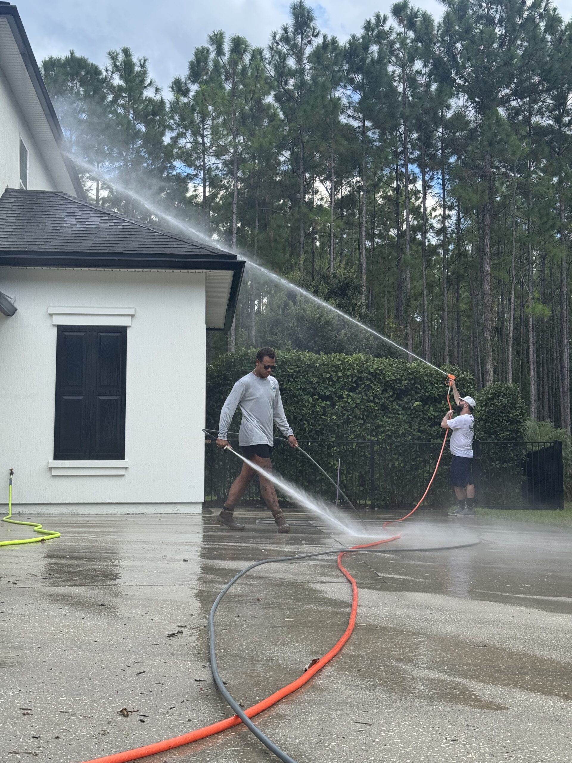 Team rinsing driveway and soft‑washing a home